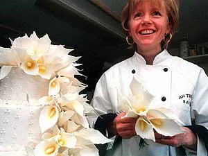 Pastry chef and owner Elizabeth Casey holding a sugar-paste flower in front of a white wedding cake