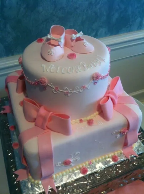 Pink fondant baby shower cake with a bow and baby shoes