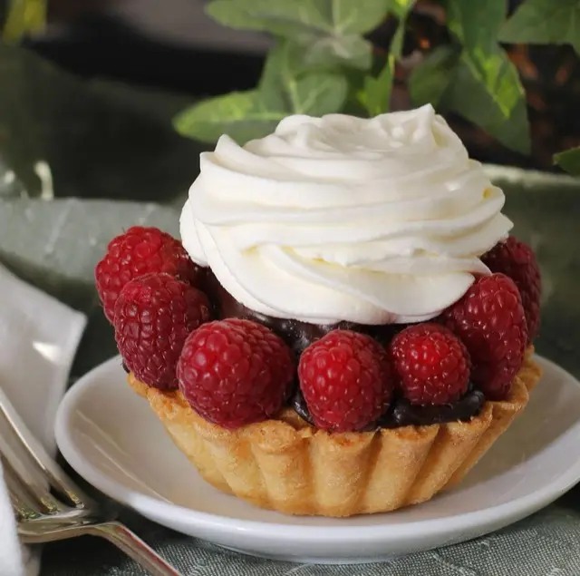 Tartlet topped with whipped cream and raspberries