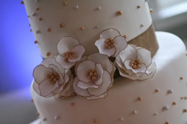 Close-up of a white wedding cake with sugar-paste flowers and gold beads